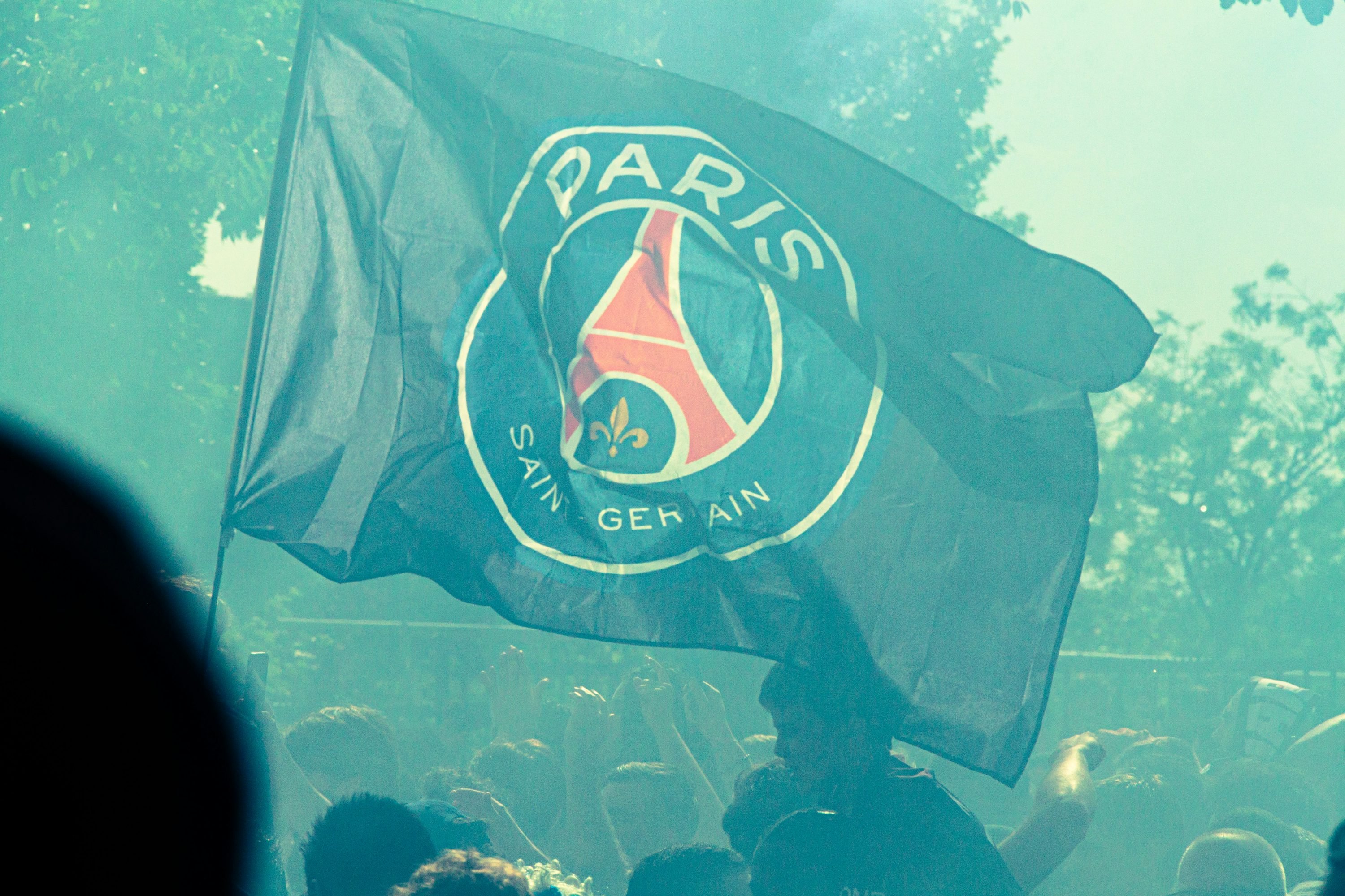 Drapeau du Paris Saint-Germain sur fond de foule lors d’un événement sportivo-football, ambiance colorée.
