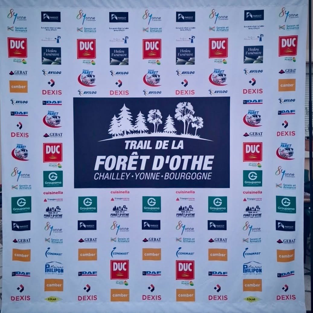 Grand panneau publicitaire personnalisé avec logo central “Trail de la Forêt d’Othe” et arbres, entouré de logos de divers sponsors en colonnes.