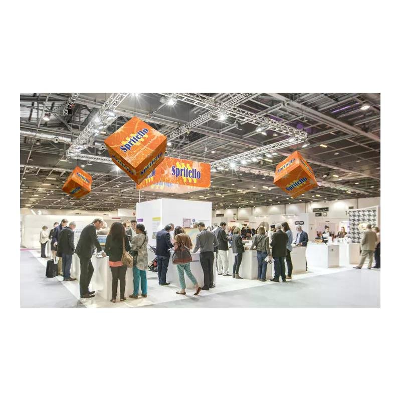 Groupe de visiteurs lors d’un salon professionnel autour de stands d’exposition, avec des modules blancs et desSuspension orange Spritello au-dessus.