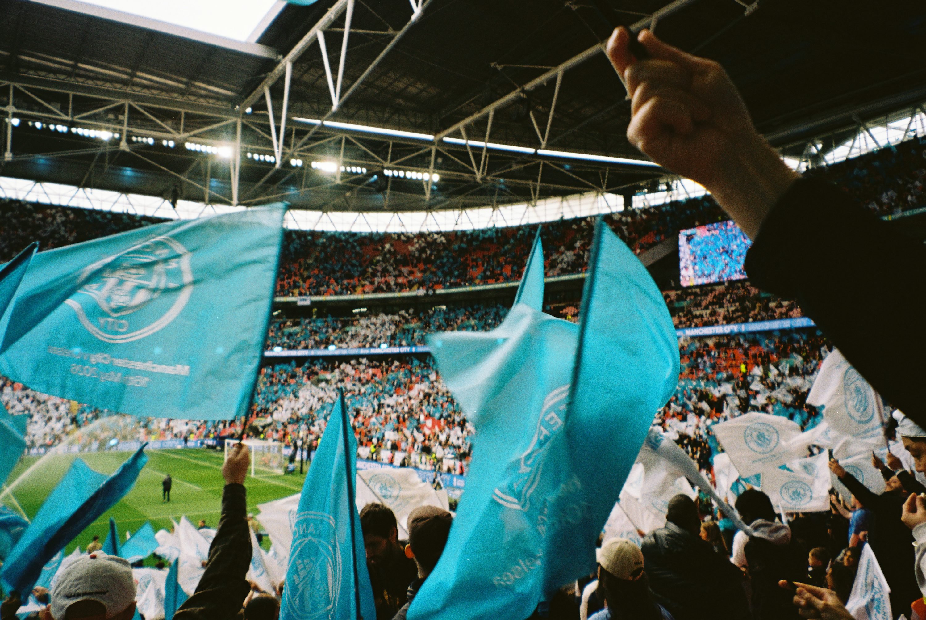 Supporters dans un stade agitant des drapeaux bleus et drapeaux blancs devant la pelouse.
