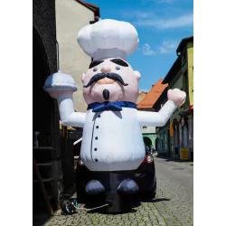 Totem gonflable en forme de chef cuisinier blanc portant toque, moustache et nœud papillon bleu sur fond de rue.